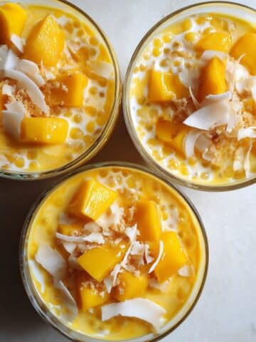 Homemade mango sago recipe in clear bowls showing creamy orange dessert with tapioca pearls. Asian tropical dessert with fresh mango chunks and coconut milk on kitchen counter.