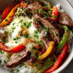 Close-up of a Philly cheesesteak bowls topped with gooey provolone cheese, tender seared steak strips, sautéed bell peppers, and fresh parsley, all served over fluffy white rice in a homemade, comforting presentation.