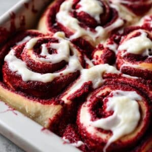Red velvet cinnamon rolls with cream cheese frosting showing deep red swirls and white icing.