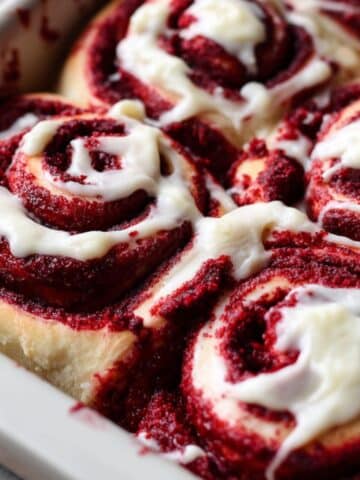 Red velvet cinnamon rolls with cream cheese frosting showing deep red swirls and white icing.