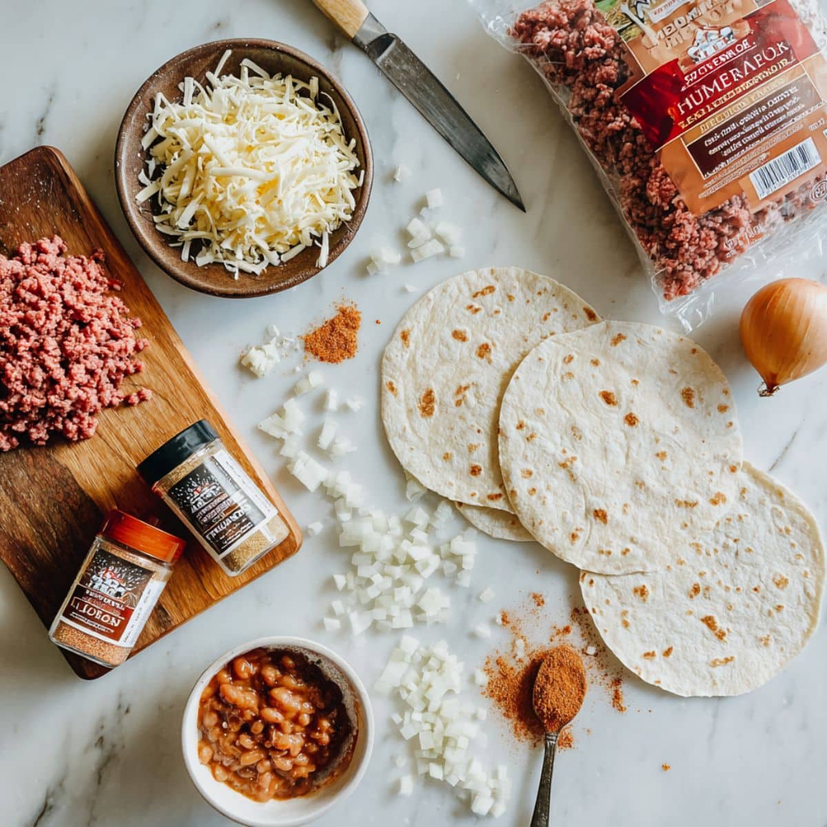 Fresh ingredients for homemade beef and cheese chimichangas including ground beef and flour tortillas.
