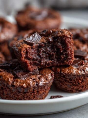 Fudgy homemade brownie bites broken in half on a white plate, revealing a gooey chocolate center with a crackly top and rich texture.