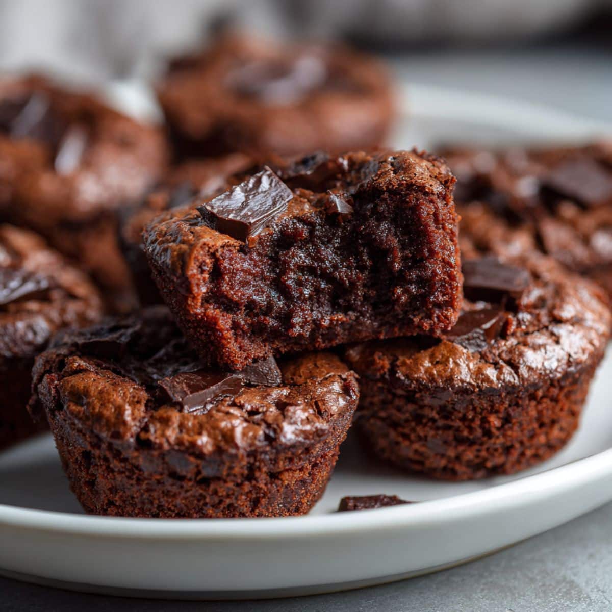 Fudgy homemade brownie bites broken in half on a white plate, revealing a gooey chocolate center with a crackly top and rich texture.