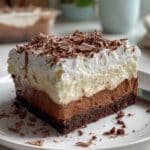 Homemade brownie refrigerator cake slice showing chocolate brownie layers with creamy pudding and whipped cream. No-bake layered dessert recipe with chocolate shavings and distinct refrigerator cake layers.