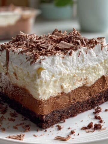 Homemade brownie refrigerator cake slice showing chocolate brownie layers with creamy pudding and whipped cream. No-bake layered dessert recipe with chocolate shavings and distinct refrigerator cake layers.