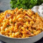 Buffalo chicken mac and cheese in ceramic bowl with creamy orange cheese sauce and fresh parsley garnish.