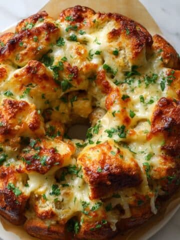 Golden cheesy chicken alfredo monkey bread with melted cheese and parsley in a bundt shape. Overhead shot on parchment-lined counter for cozy dinner vibes.