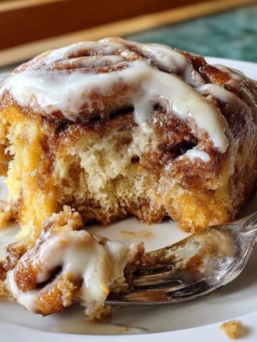 Gooey cinnamon roll cake slice with cream cheese glaze dripping down golden brown layers