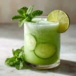 Refreshing cucumber lime agua fresca served over ice in a clear glass, garnished with fresh mint, lime slice, and cucumber rounds.