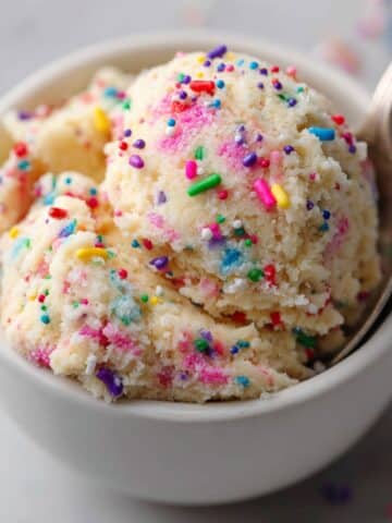 Tasty edible sugar cookie dough scoop with rainbow sprinkles in a white bowl, served with a spoon and soft natural lighting for a cozy homemade look.