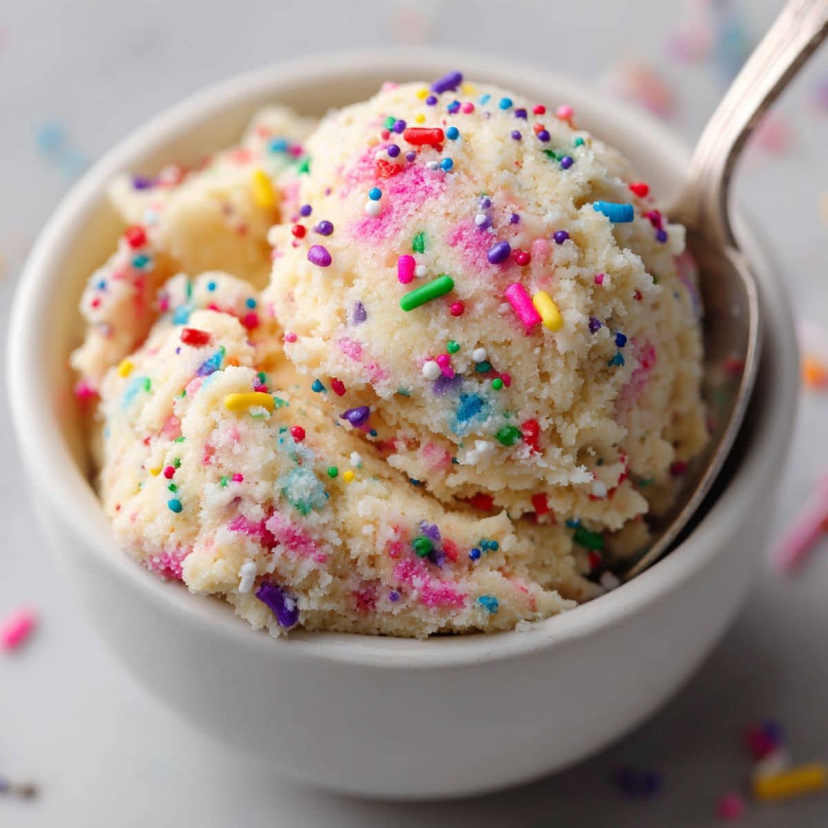 Tasty edible sugar cookie dough scoop with rainbow sprinkles in a white bowl, served with a spoon and soft natural lighting for a cozy homemade look.