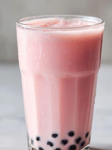 Chilled glass of fresh strawberry milk tea with a creamy pink hue and chewy black tapioca pearls, served over ice for a sweet and refreshing boba drink experience.
