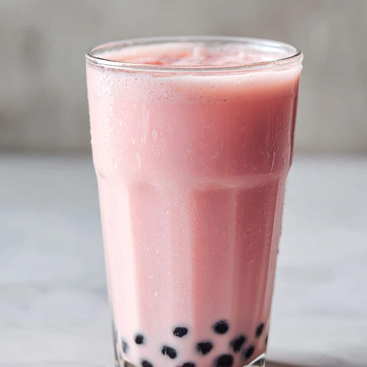 Chilled glass of fresh strawberry milk tea with a creamy pink hue and chewy black tapioca pearls, served over ice for a sweet and refreshing boba drink experience.