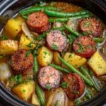 Hearty crockpot kielbasa and green beans with golden potatoes, caramelized onions, and smoked sausage slices, all coated in a savory broth and topped with fresh parsley for a rustic, homemade comfort dish.