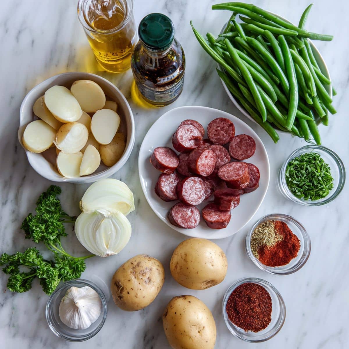 All ingredients for kielbasa and green beans laid out casually on a white kitchen counter. Includes sausage, potatoes, green beans, spices, and fresh garlic.