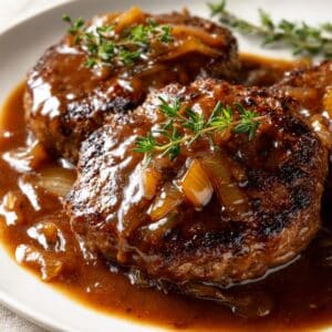 Close-up of old-fashioned Salisbury steak smothered in rich brown onion gravy, served with fresh thyme on top.
