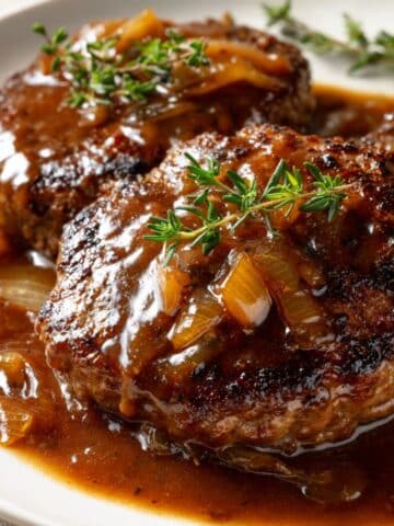 Close-up of old-fashioned Salisbury steak smothered in rich brown onion gravy, served with fresh thyme on top.