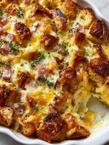 Golden-baked savory bread pudding with ham, cheese, and herbs in a white scalloped dish, crispy on top and soft inside