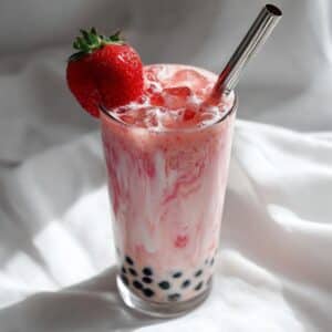 Creamy strawberry milk tea swirled with real fruit and chewy boba pearls, served in a tall glass with a metal straw and fresh strawberry garnish. A vibrant and refreshing pink drink perfect for summer.