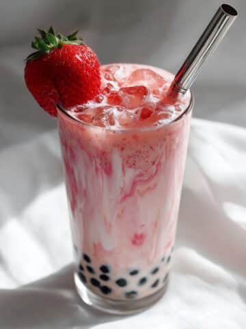 Creamy strawberry milk tea swirled with real fruit and chewy boba pearls, served in a tall glass with a metal straw and fresh strawberry garnish. A vibrant and refreshing pink drink perfect for summer.