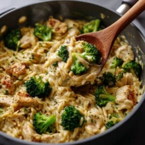 creamy chicken broccoli orzo in a skillet, with tender chicken chunks, golden orzo pasta, and bright green broccoli scooped up on a wooden spoon, glossy and homemade.