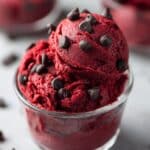 Edible red velvet cookie dough served in a clear glass cup, rich red color with a creamy soft texture and topped with semi-sweet chocolate chips. A homemade no-bake red velvet dessert recipe that’s safe to eat, indulgent, and perfect for chocolate lovers.