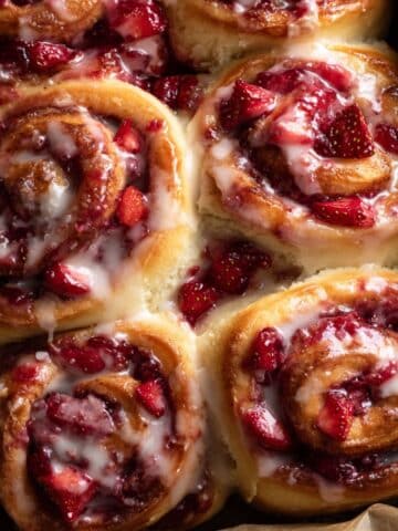 Homemade strawberry cinnamon rolls with glossy icing and fresh strawberry filling, close-up view of soft, fluffy dough swirled with jam and topped with a creamy glaze.