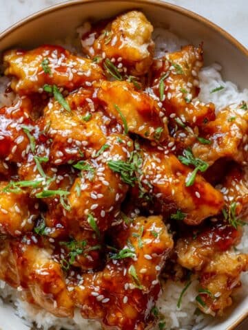 Glossy sweet chili chicken glazed in a sticky homemade sauce, served over white rice and topped with sesame seeds and chopped green onions for a flavorful, mouthwatering dinner bowl.