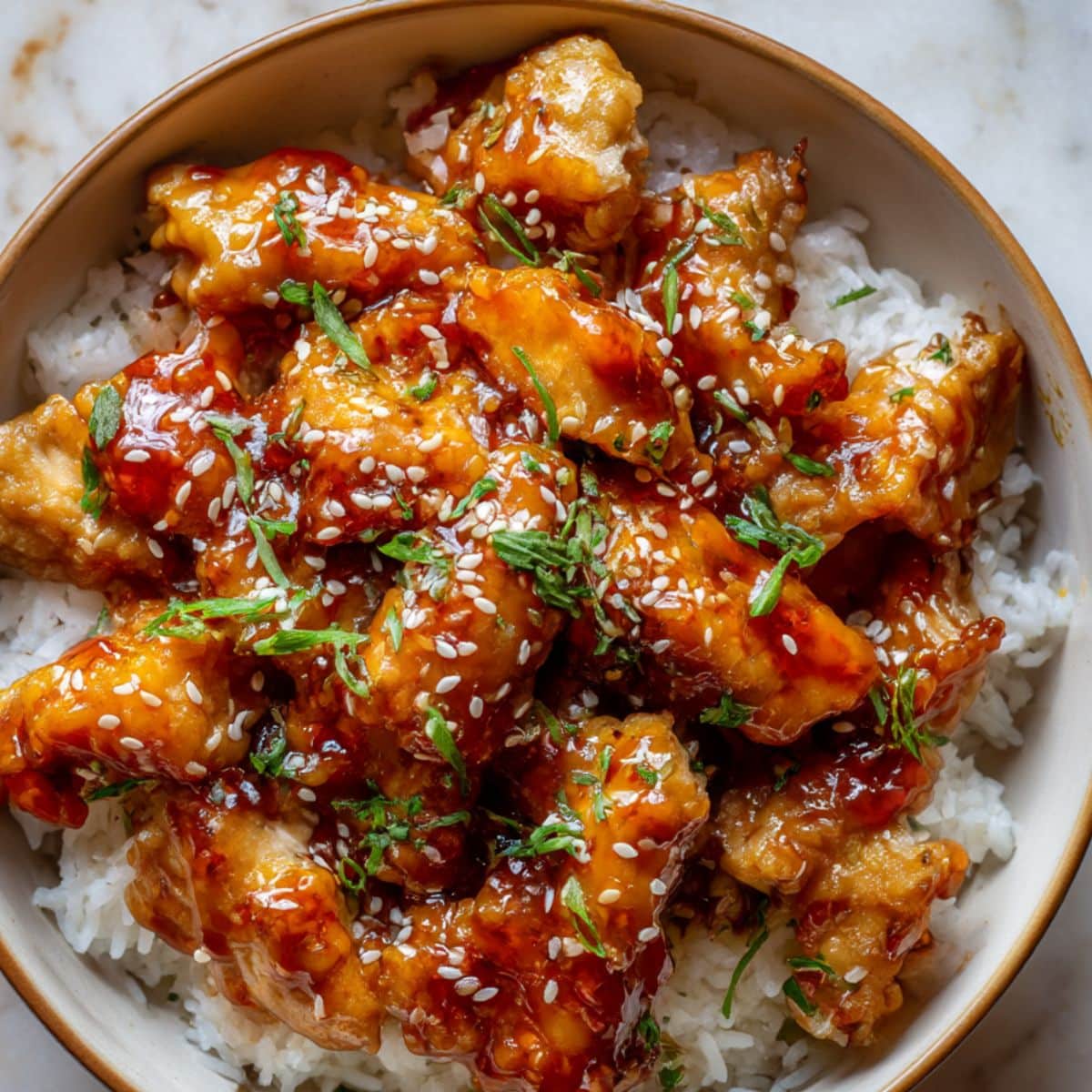 Glossy sweet chili chicken glazed in a sticky homemade sauce, served over white rice and topped with sesame seeds and chopped green onions for a flavorful, mouthwatering dinner bowl.
