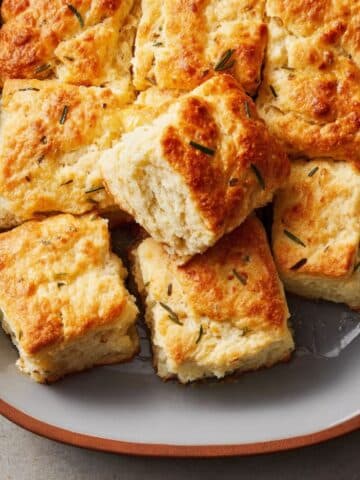golden-baked butter swim biscuits in a white ceramic pan, cut into neat squares with lightly crisped tops and soft, fluffy centers, one piece pulled out showing a tender crumb, minimal melted butter pooling in the corner, styled on a neutral countertop with natural daylight.