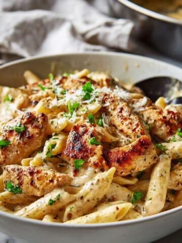 Creamy garlic parmesan chicken pasta served in a white bowl on a marble counter, made with penne pasta, juicy seared chicken strips, rich garlic parmesan sauce, fresh parsley, and grated parmesan cheese.