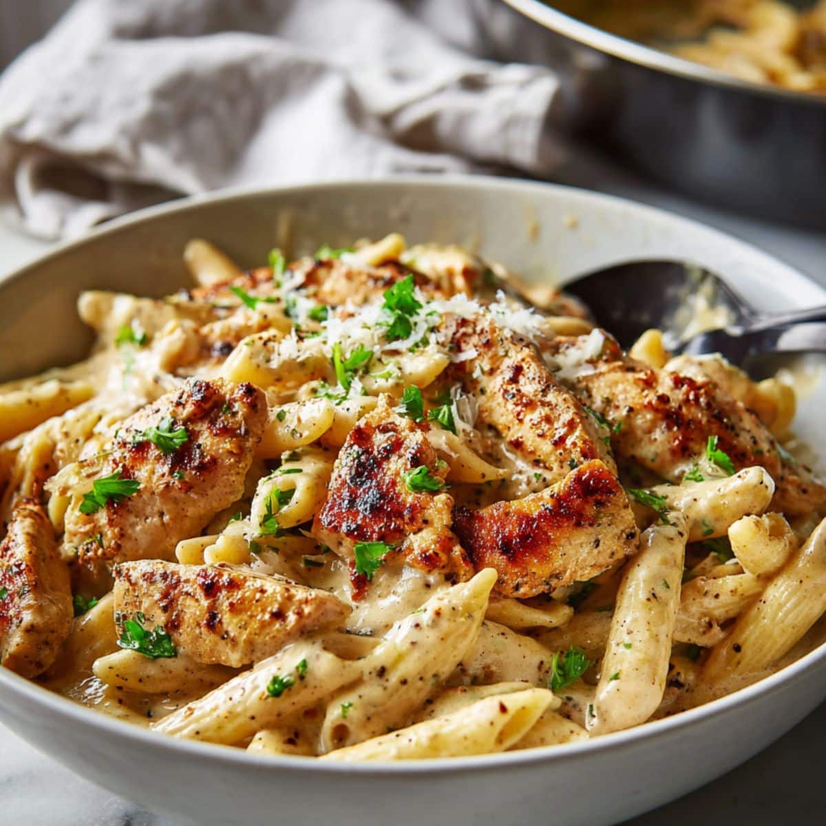 Creamy garlic parmesan chicken pasta served in a white bowl on a marble counter, made with penne pasta, juicy seared chicken strips, rich garlic parmesan sauce, fresh parsley, and grated parmesan cheese.