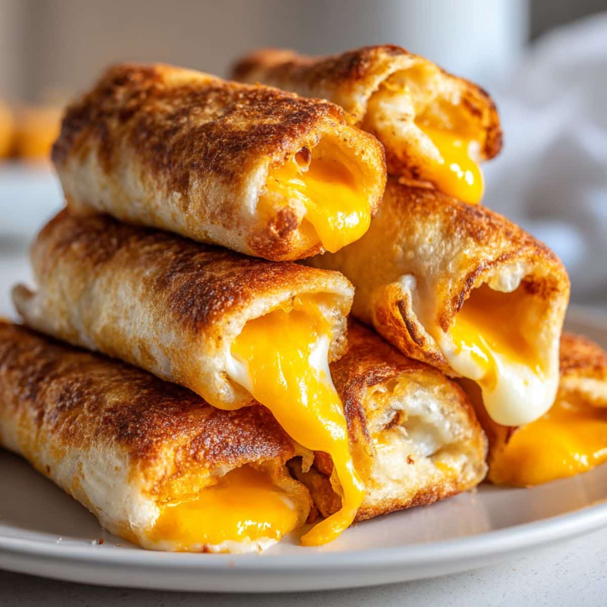 Golden brown grilled cheese roll-ups stacked on a white plate, made with crispy toasted bread and gooey melted American cheese oozing out of the ends.