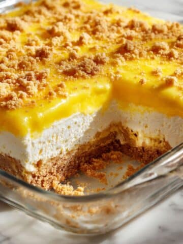 Side view of a golden lemon cream cheese dump cake in a glass baking dish, showing layers of buttery crumb crust, creamy filling, and glossy lemon topping with crumbles, baked to perfection for a rich, tangy, and homemade dessert.