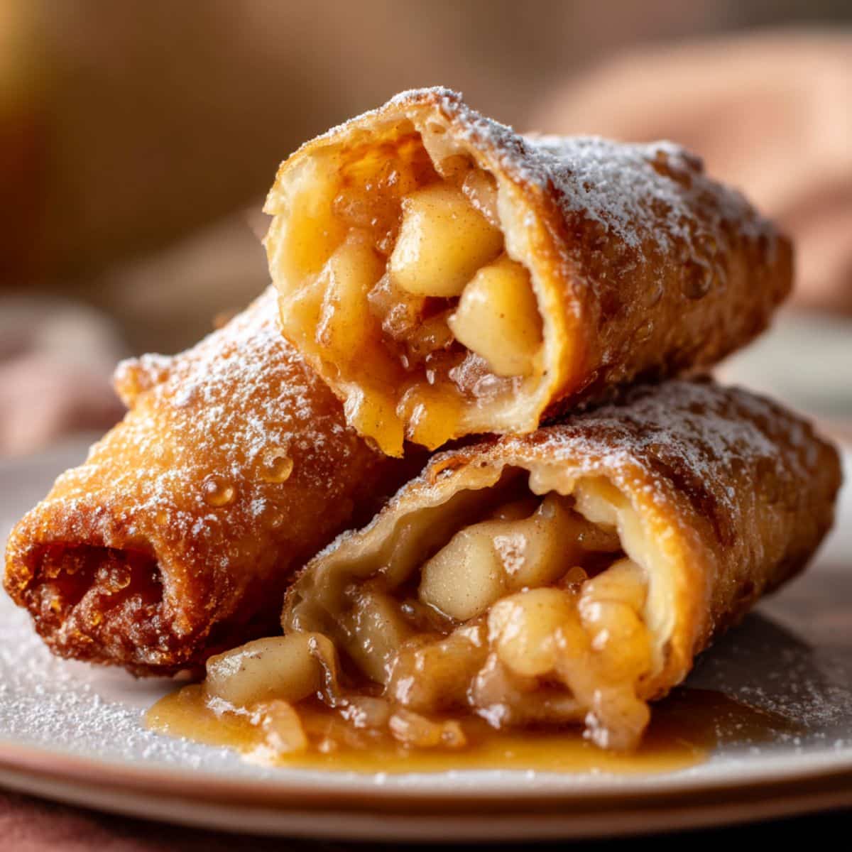 Golden brown apple pie egg rolls filled with warm cinnamon-spiced apple chunks, drizzled with glossy caramel sauce and dusted with powdered sugar for a crispy, gooey, and mouthwatering dessert.