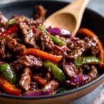 Close-up of Chinese pepper steak with tender beef strips coated in glossy brown sauce, stir-fried with bright red, green, and orange peppers for a colorful, mouthwatering dish.