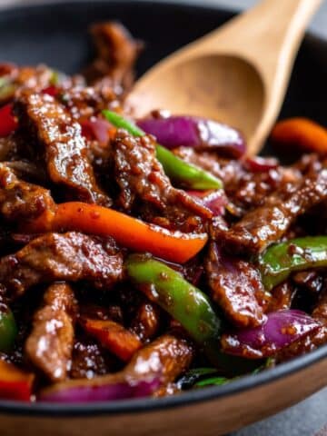 Close-up of Chinese pepper steak with tender beef strips coated in glossy brown sauce, stir-fried with bright red, green, and orange peppers for a colorful, mouthwatering dish.