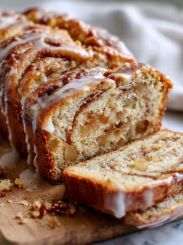 Cinnamon swirl apple fritter bread sliced showing golden interior with glaze and apple chunks with swirl pattern.