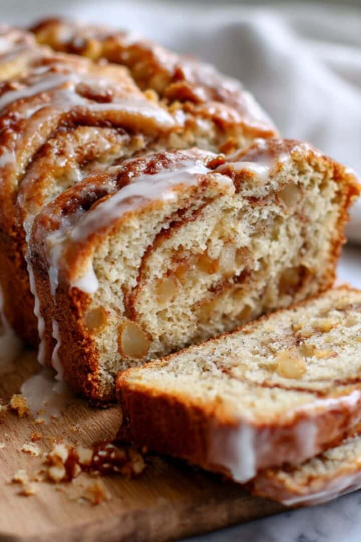 Cinnamon swirl apple fritter bread sliced showing golden interior with glaze and apple chunks with swirl pattern.