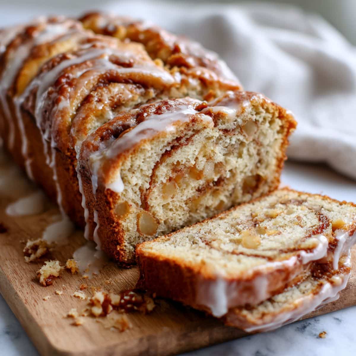 Cinnamon swirl apple fritter bread sliced showing golden interior with glaze and apple chunks with swirl pattern.