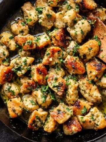 Golden garlic butter chicken bites in cast iron skillet with fresh parsley and melted butter.