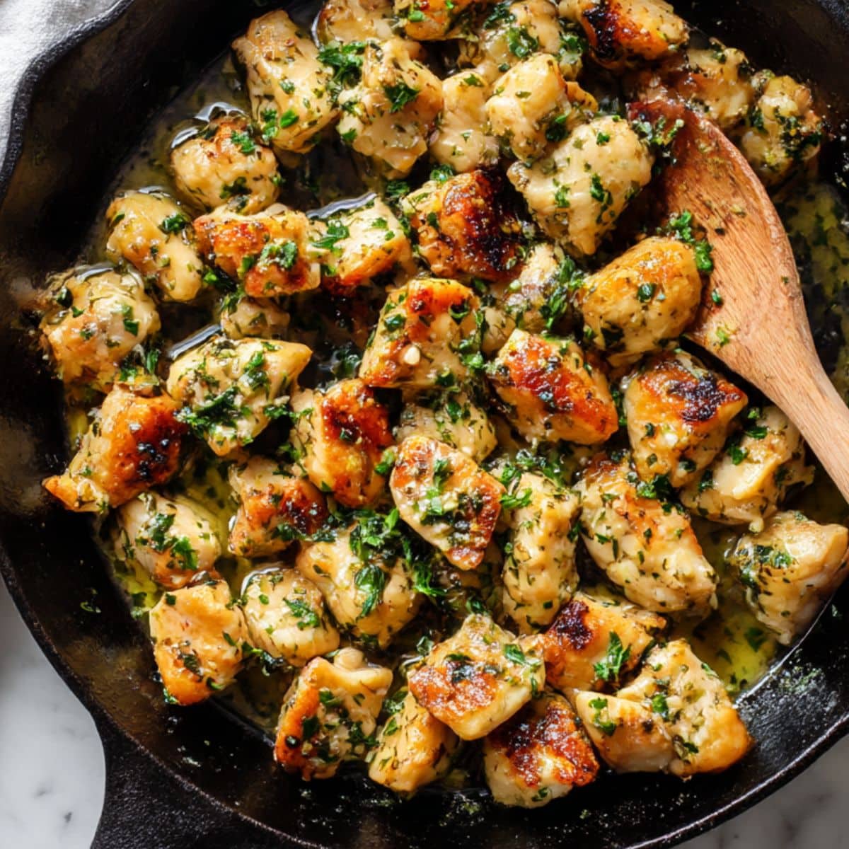 Golden garlic butter chicken bites in cast iron skillet with fresh parsley and melted butter.