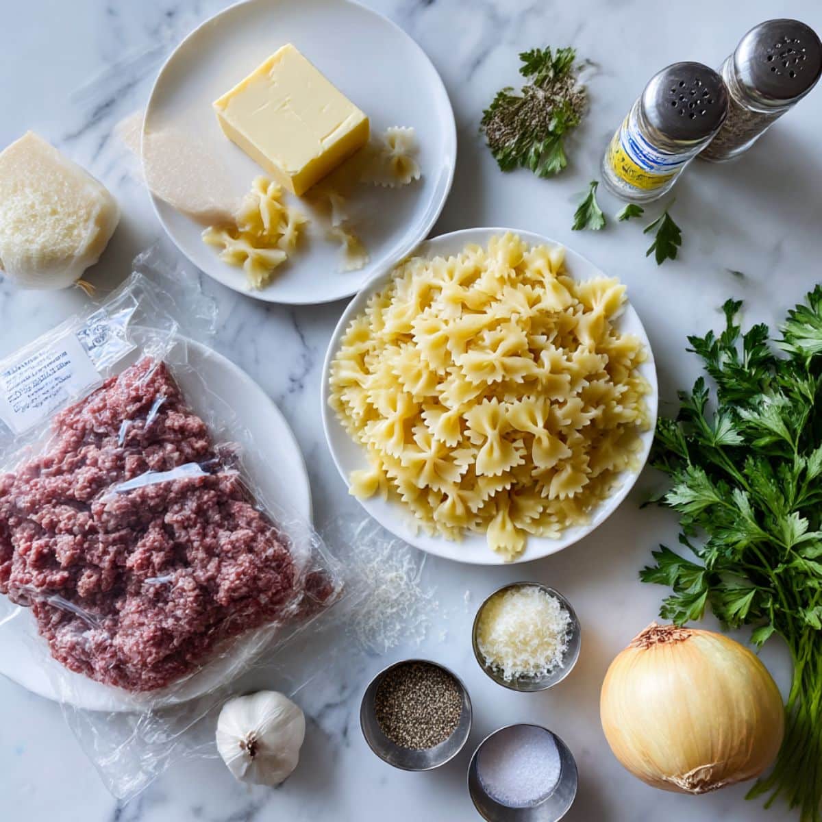 All ingredients for creamy beef and bowtie pasta including farfalle, ground beef, heavy cream and parmesan cheese.