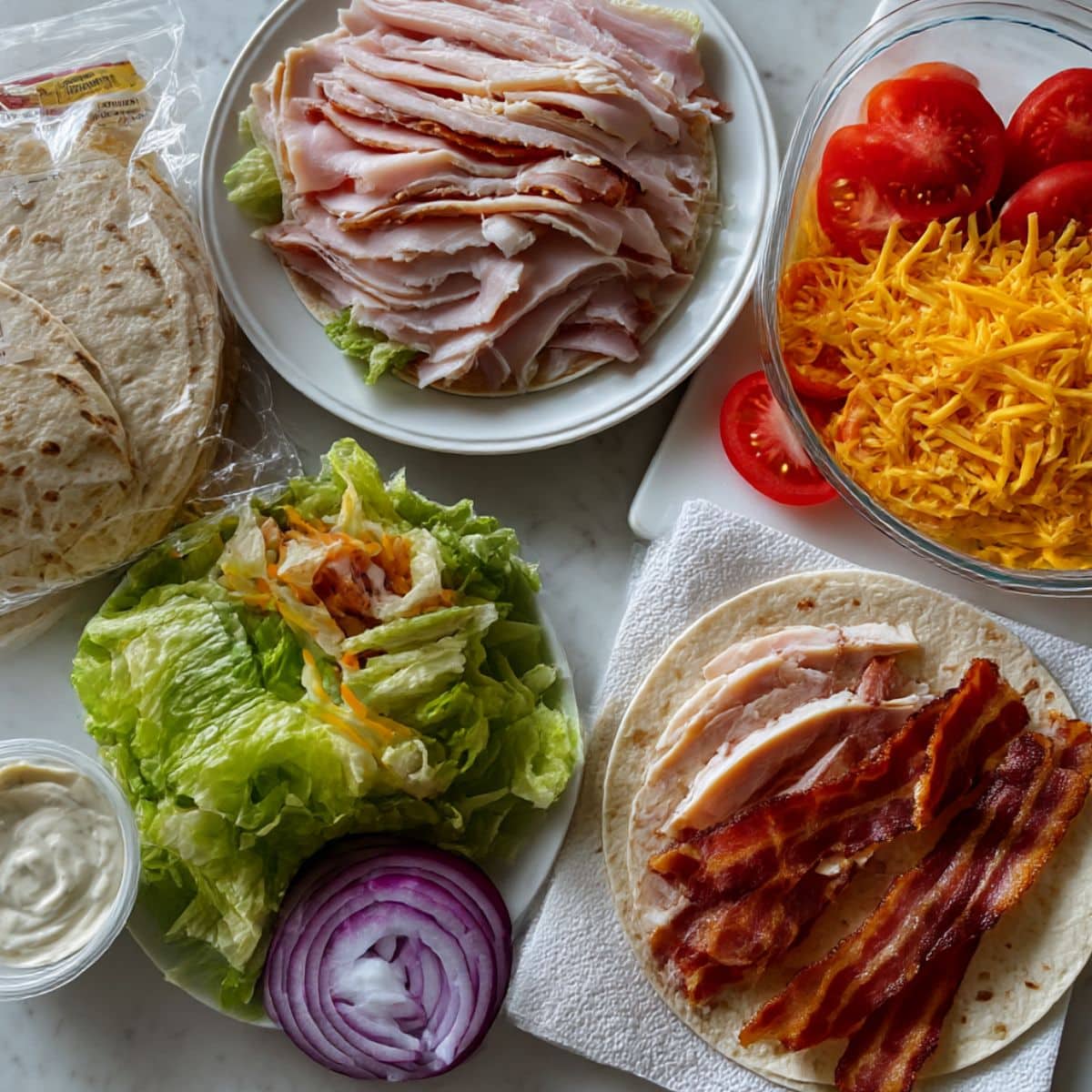 All ingredients for turkey club wrap including deli turkey, bacon, lettuce, tomatoes and ranch dressing.