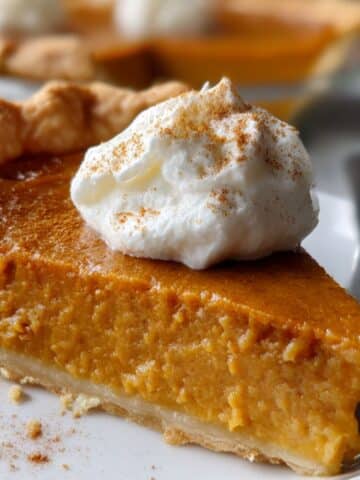 Baked libby's pumpkin pie recipe slice with smooth golden filling and whipped cream dollop on white plate.