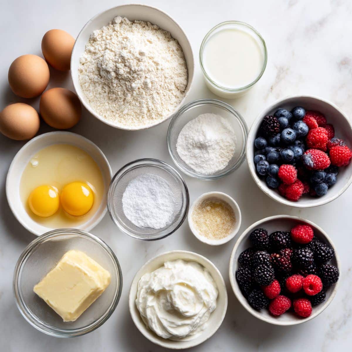 fresh pancake tacos ingredients including flour, eggs, milk, cream, and colorful mixed berries arranged on a white kitchen counter for a homemade breakfast prep scene.