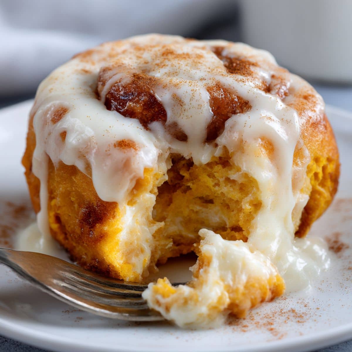 Moist pumpkin cinnamon roll with vibrant orange dough, topped with melted cream cheese frosting and gooey cinnamon filling on a white plate.