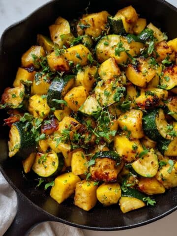 Roasted zucchini and squash in cast iron skillet showing golden-brown caramelized edges and fresh herbs.
