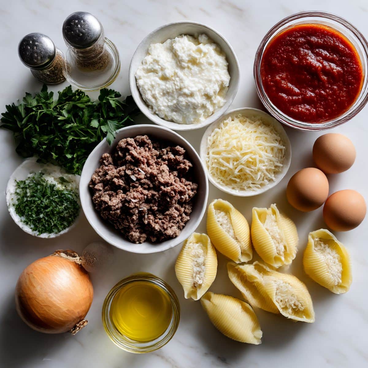 Complete ingredients for stuffed shells recipe including jumbo pasta, ricotta cheese, ground beef, and marinara sauce.