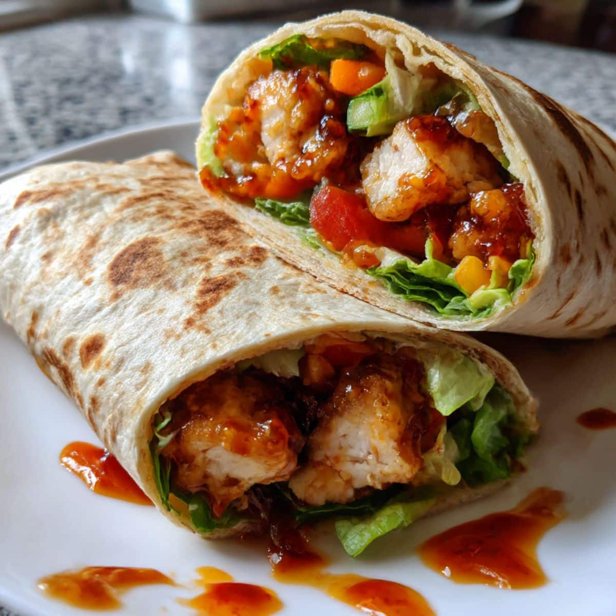 Sweet chili chicken wrap cut in half showing glazed chicken pieces and fresh vegetables in golden tortilla.